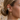 Close-up of a woman's ear wearing multiple earrings, including a gold cone drop earring with small clear stones, a gold hoop, a cluster of turquoise and white stones, a small star-shaped stud, and a curved bar, against a softly blurred stone wall.