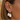 A close-up of a person's ear wearing a stack of gold and pearl jewelry, featuring two gold huggie hoop earrings with large baroque-style white pearls dangling from them, along with a small pearl stud and a tiny floral cluster stud.
